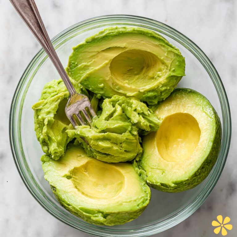 Creamy avocado halves with a fork in a glass bowl, vibrant green.