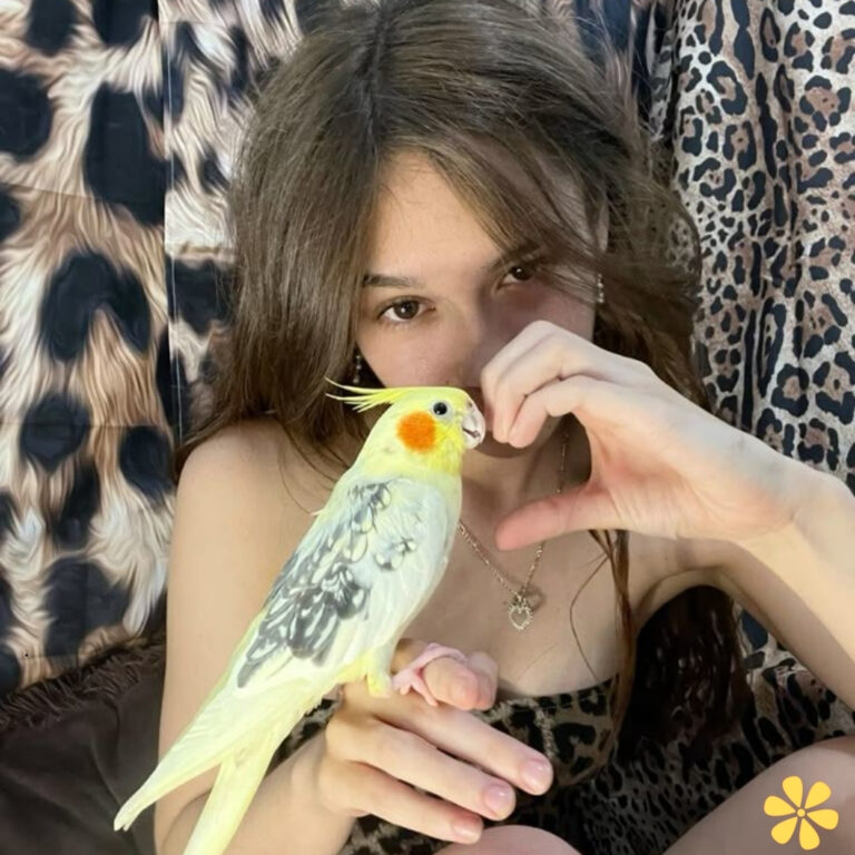 Girl making a heart shape with her hand, holding a yellow bird on her lap.