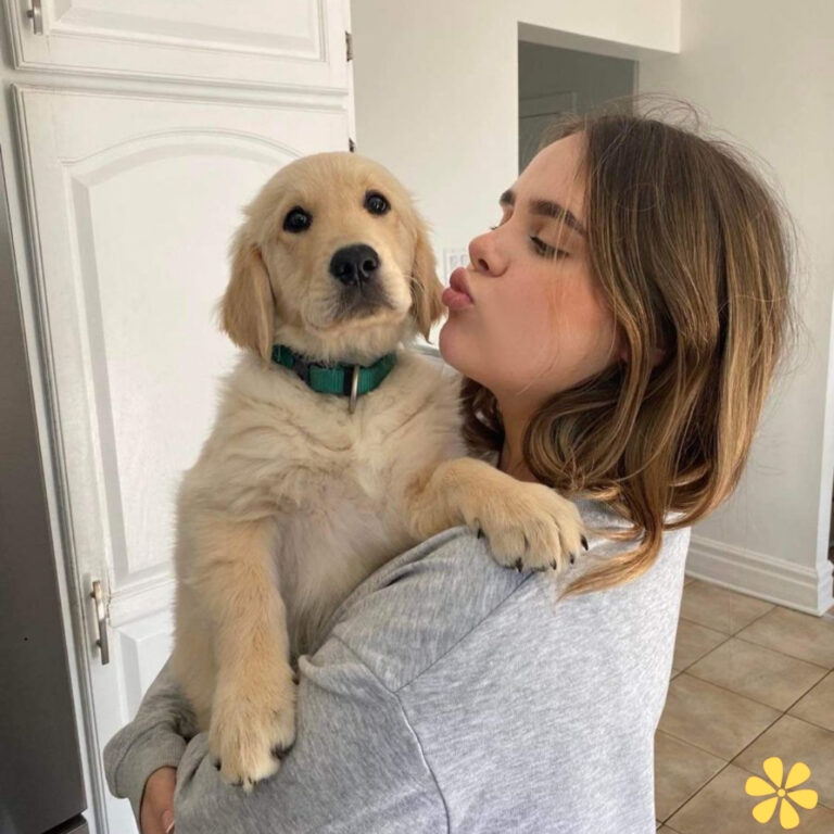 A person with short hair kisses a golden retriever puppy, smiling warmly.