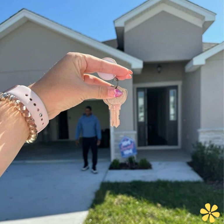 A hand holding a set of keys in front of a new house.