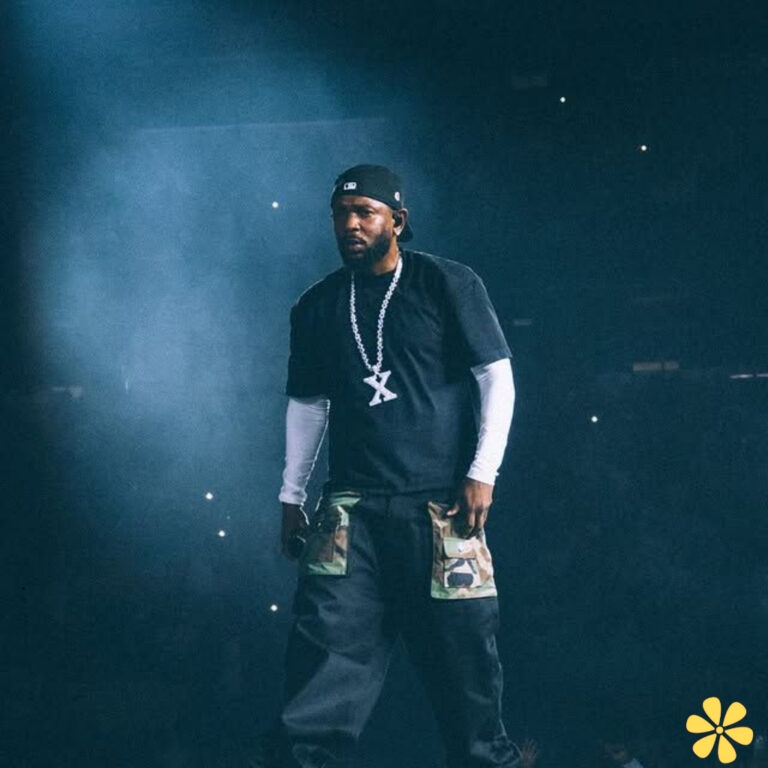 A performer on stage, wearing a black shirt and camo pants, illuminated by stage lights.