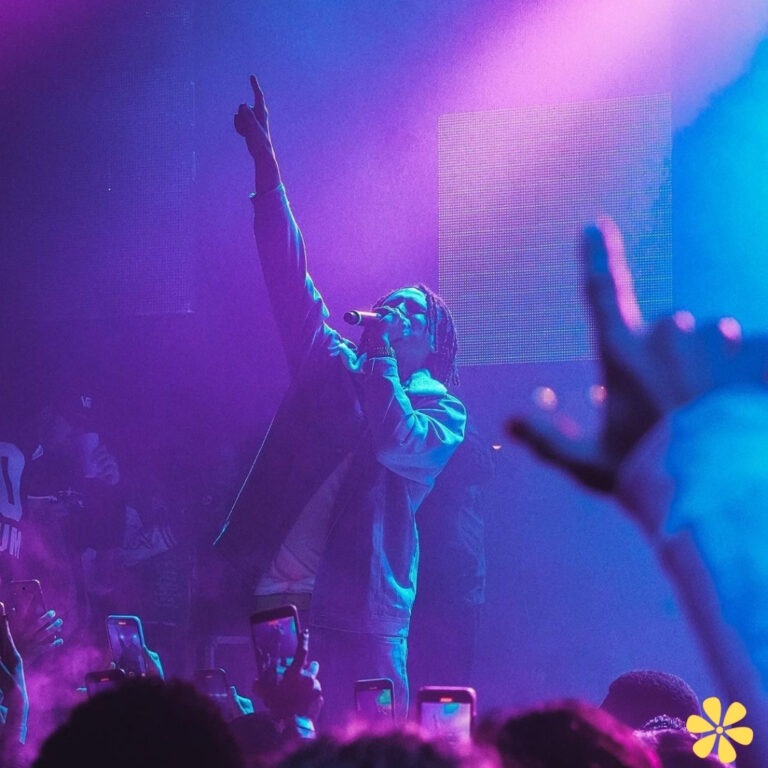 A performer passionately sings to a vibrant crowd, illuminated by purple and pink lights.