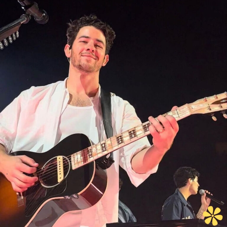 A musician with a guitar smiles at the audience during a performance.