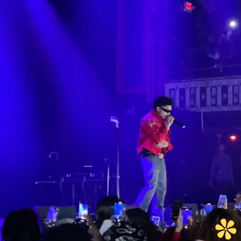 A performer in a red shirt sings passionately on stage, illuminated by blue lights.