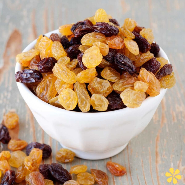A white bowl overflowing with golden and dark raisins on a rustic wooden surface.