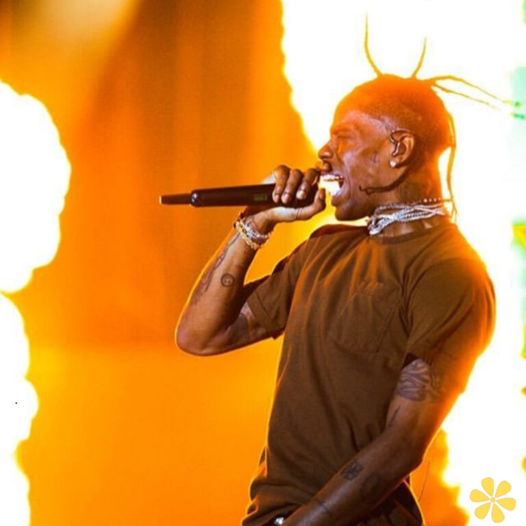 A performer passionately singing into a microphone with flames behind him.