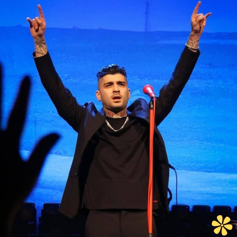 Man with tattoos raises arms in excitement on stage, microphone in front.