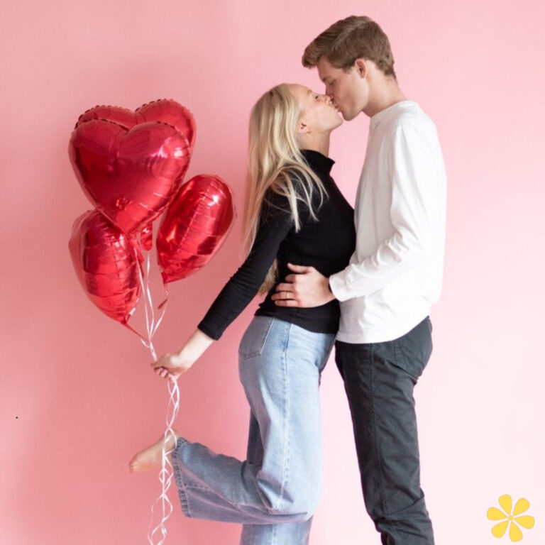 Couple kissing with heart-shaped balloons against a pink backdrop.