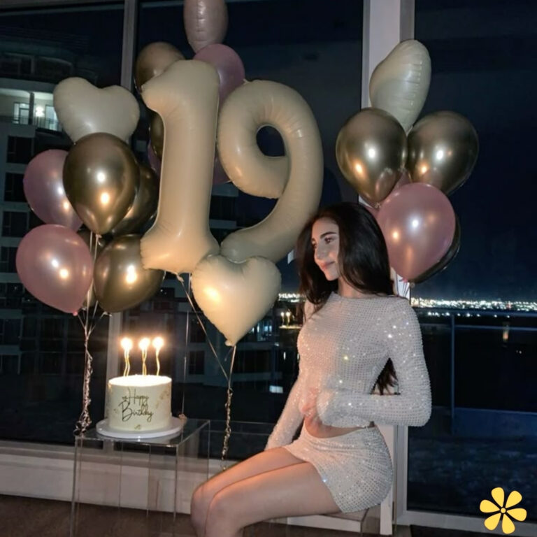 A young woman in a sparkly dress sits beside a birthday cake and balloons, celebrating her 19th birthday.