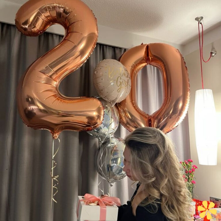 A woman with long, wavy hair stands beside large rose gold balloons reading '20'.