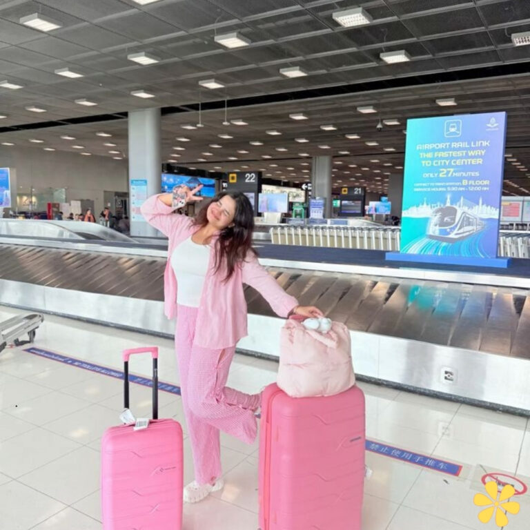 A traveler playfully poses at the airport with pink luggage, exuding excitement and joy.