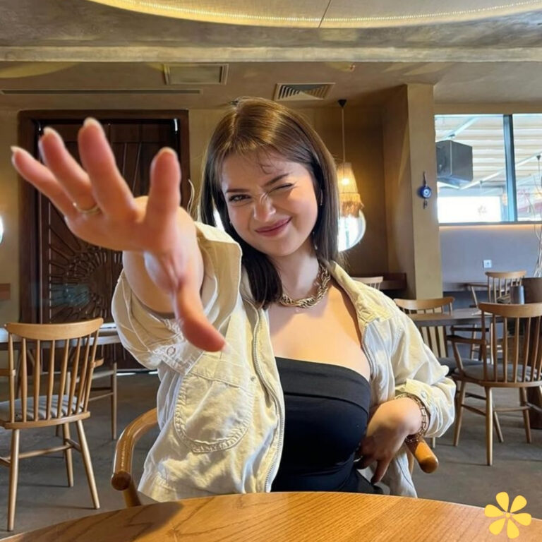 A smiling woman playfully reaching out with her hand, seated in a cozy restaurant.