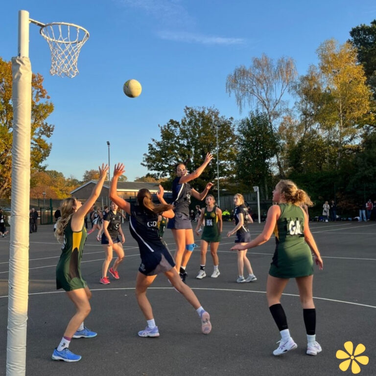 Players in action during a netball game, with one jumping to shoot.