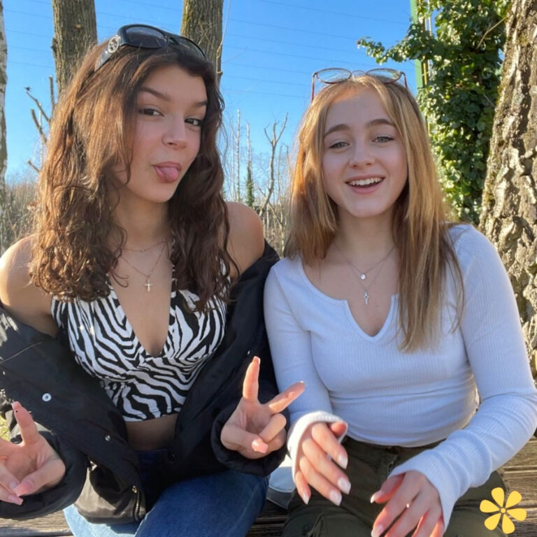 Two friends smile and pose playfully outdoors, wearing trendy outfits and enjoying the sun.