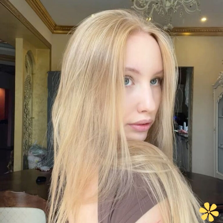 A young woman with long blonde hair looks over her shoulder, revealing a soft expression.