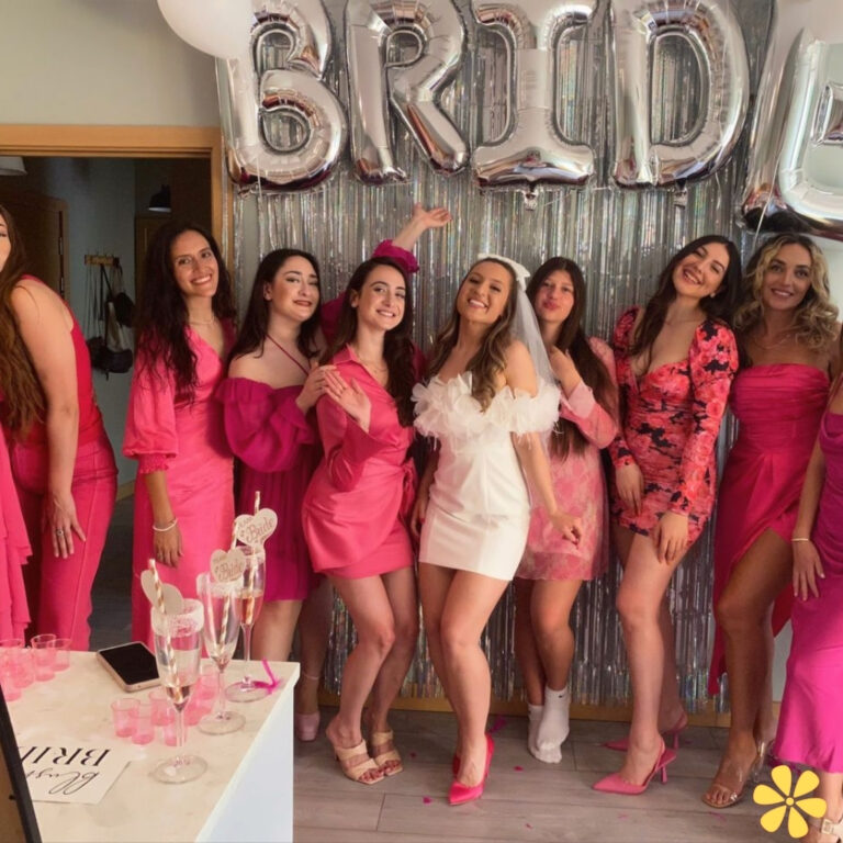 Group of women in pink outfits celebrating a bridal party with balloons and drinks.