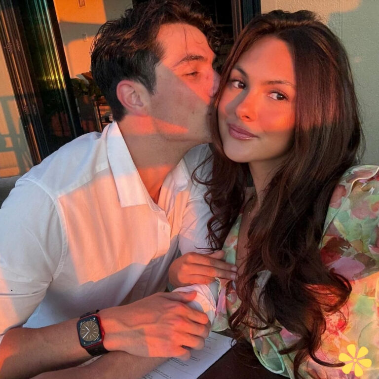 Couple sharing a sweet moment, with one person kissing the other on the cheek as sunlight bathes them in warm tones.