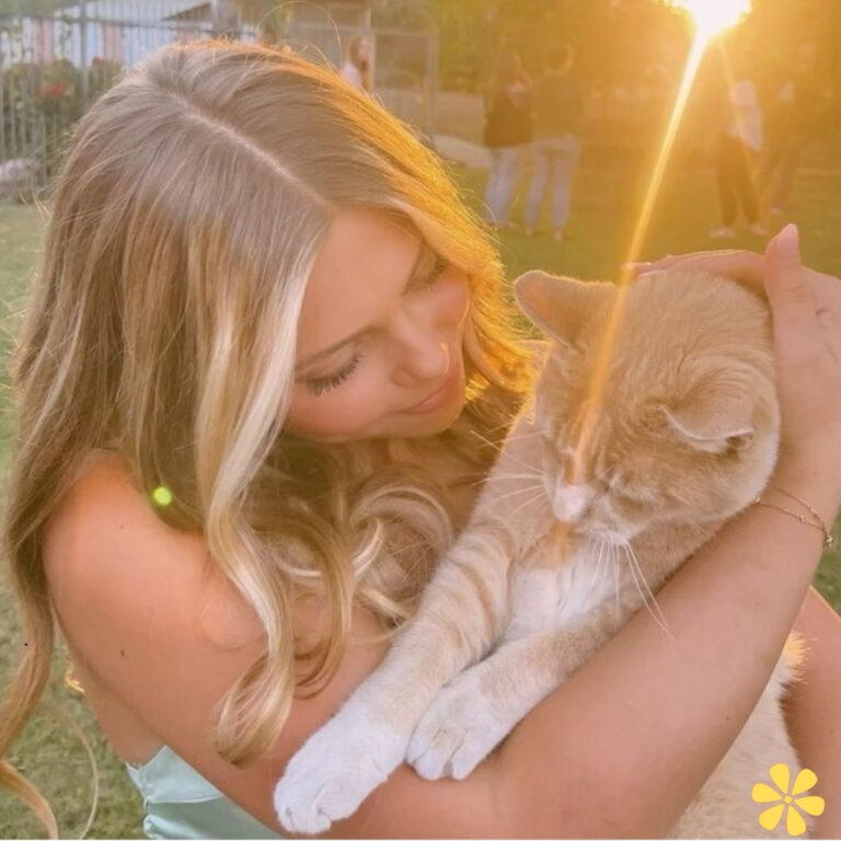A woman gently cradles a light orange cat in her arms, smiling softly at it.
