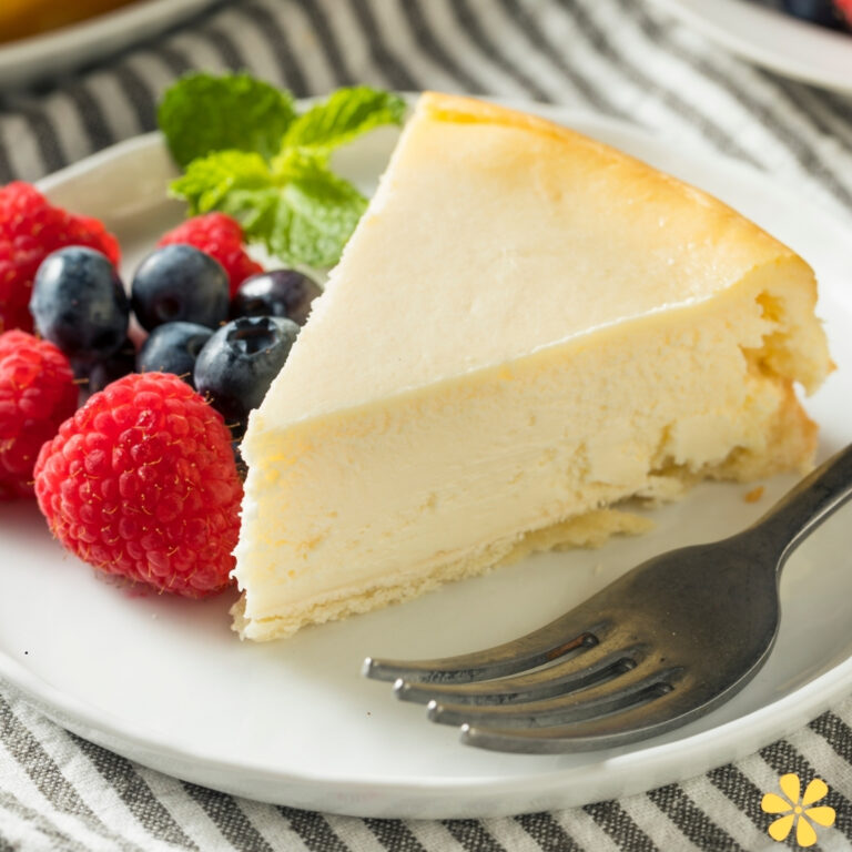 Creamy cheesecake slice on a plate with fresh raspberries, blueberries, and mint leaves.