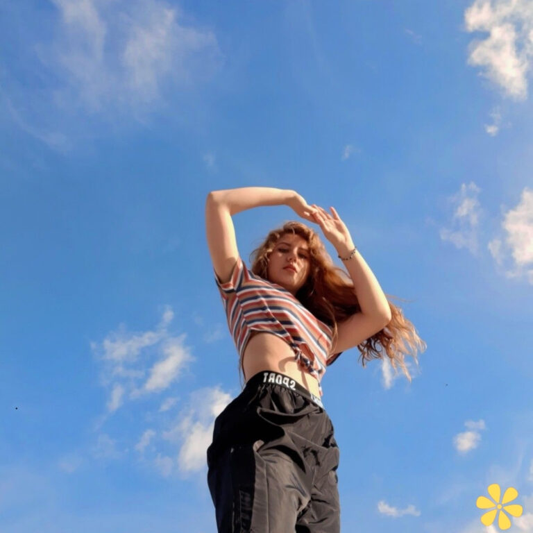 A young woman with flowing hair poses confidently against a bright blue sky.