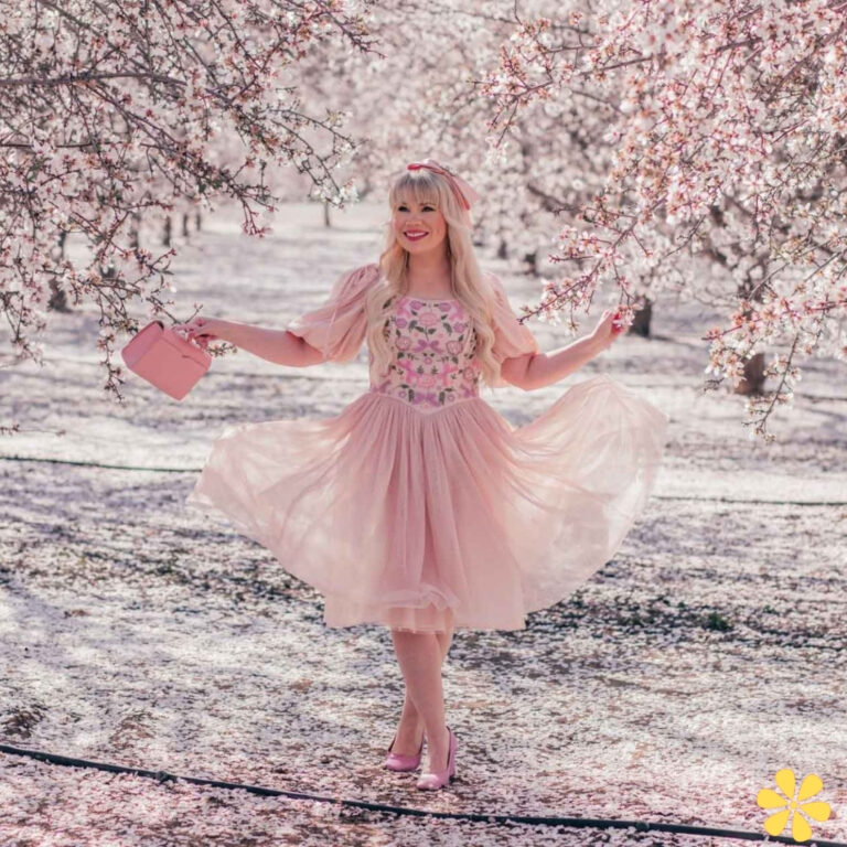 A joyful woman in a pink floral dress twirls under blossoming trees.