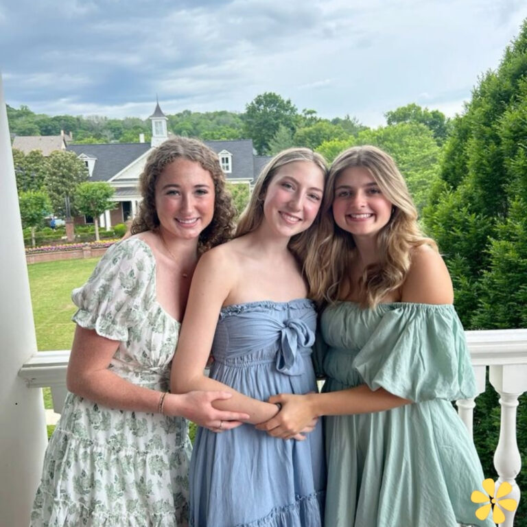 Three friends smiling together on a porch, enjoying a sunny day.