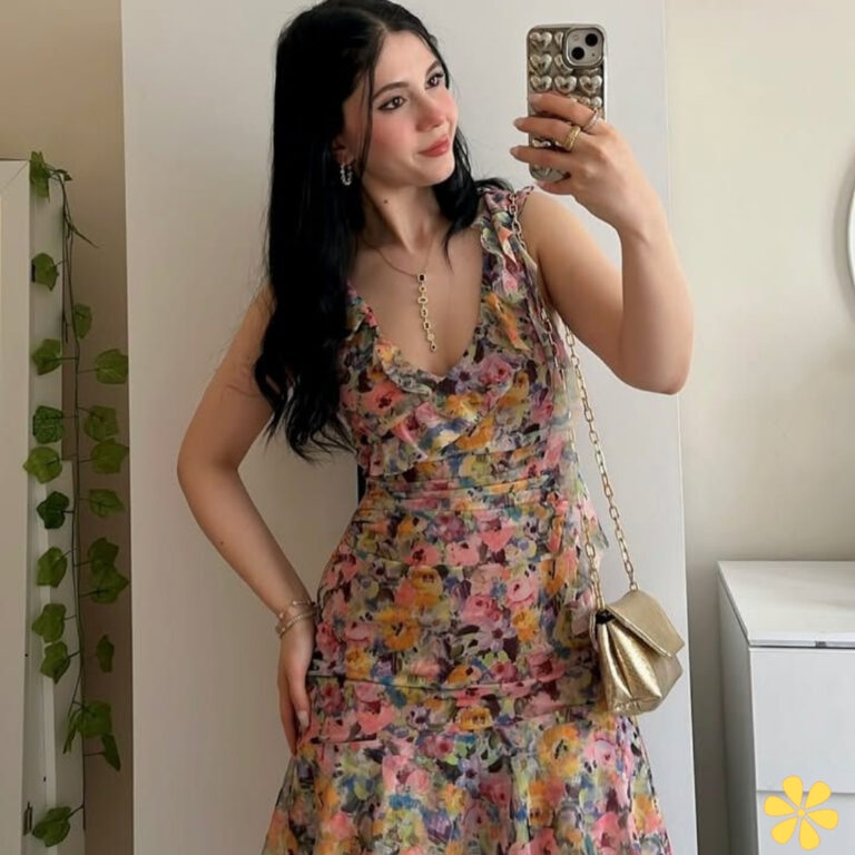 A woman in a floral dress smiles while taking a selfie, exuding confidence.