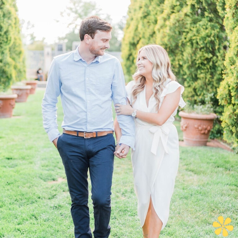 Couple strolls hand in hand through a green garden, sharing smiles.