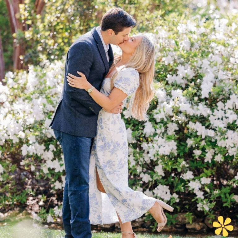 Couple sharing a kiss in a blooming garden, surrounded by white flowers.