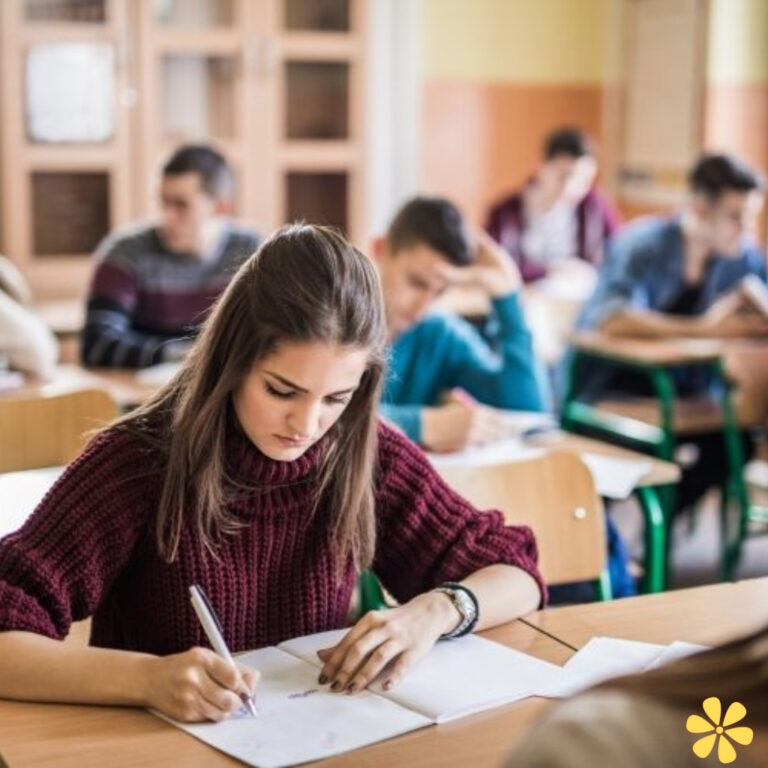 Student focused on writing in a classroom, classmates in the background.