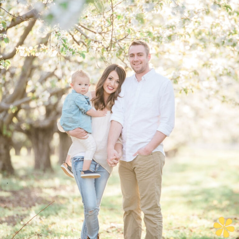 Family stands together under blooming trees, enjoying a sunny day in nature.