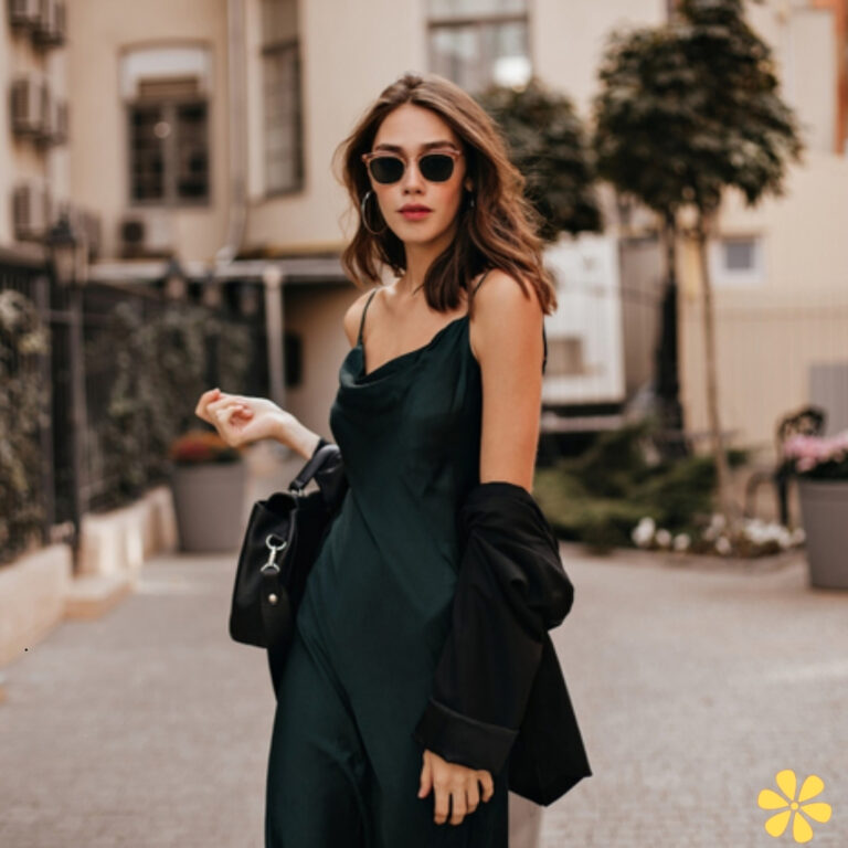 A woman in a stylish dark green dress, wearing sunglasses, holds a bag, exuding confidence.