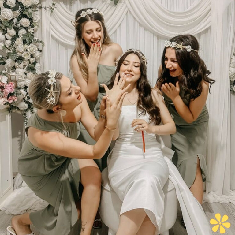 A bride in a white dress surrounded by friends in green dresses, all smiling and celebrating.