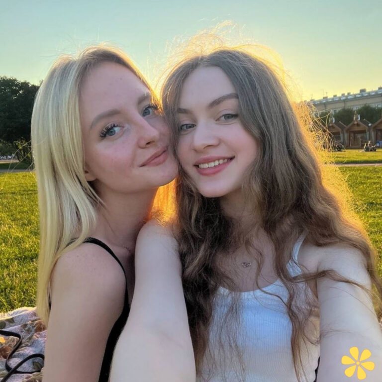 Two young women smiling warmly, enjoying a sunny day in a park, with soft sunlight illuminating their hair.