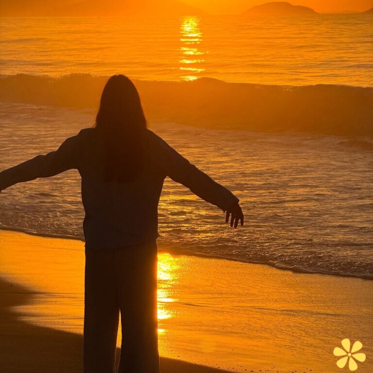 Silhouette of a person with outstretched arms against a stunning sunset over the ocean.