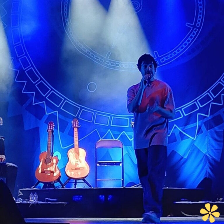 Musician performing on stage with guitars in the background, illuminated by blue lights.