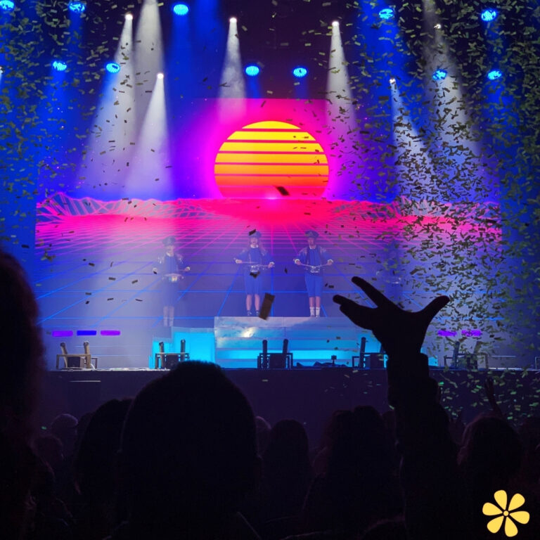 Three performers on stage, colorful lights and confetti enhance the atmosphere.