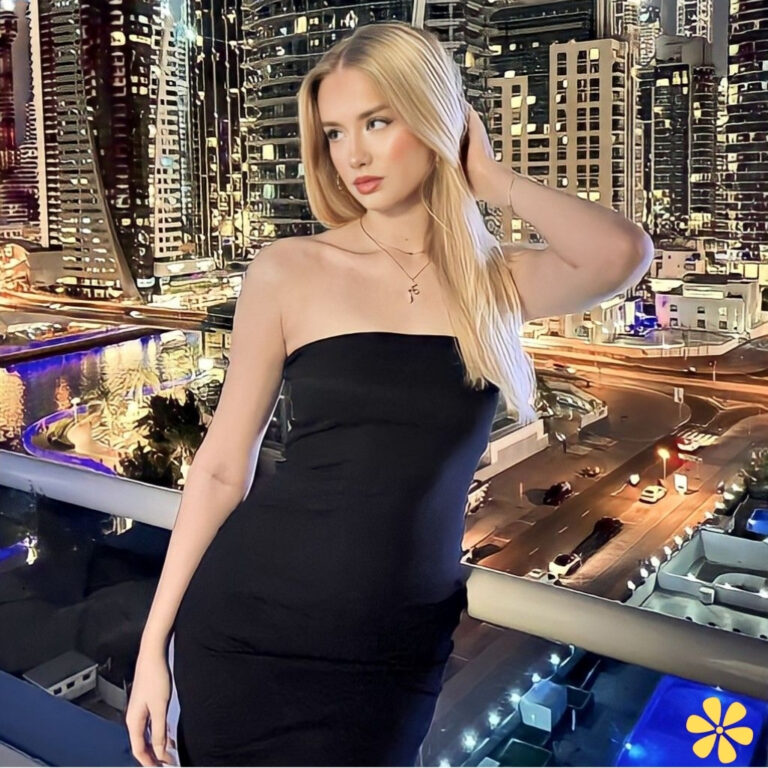 A woman with long blonde hair poses in a sleek black dress, city lights shimmering behind her.
