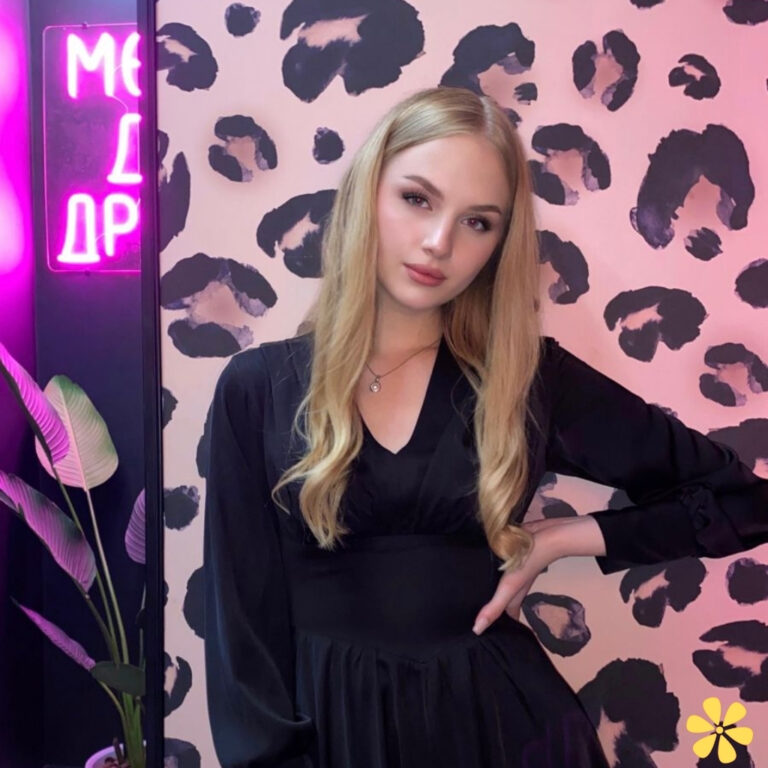 A young woman poses confidently in a black dress against a bold leopard print wall, with neon lights glowing.