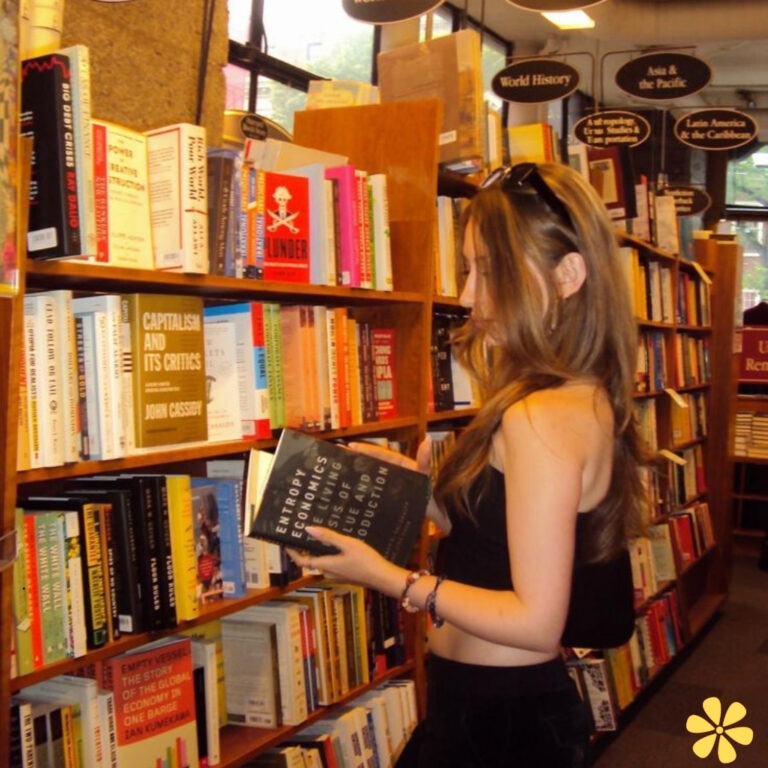 Woman browsing bookshelves, holding titles on economics, warm bookstore atmosphere.