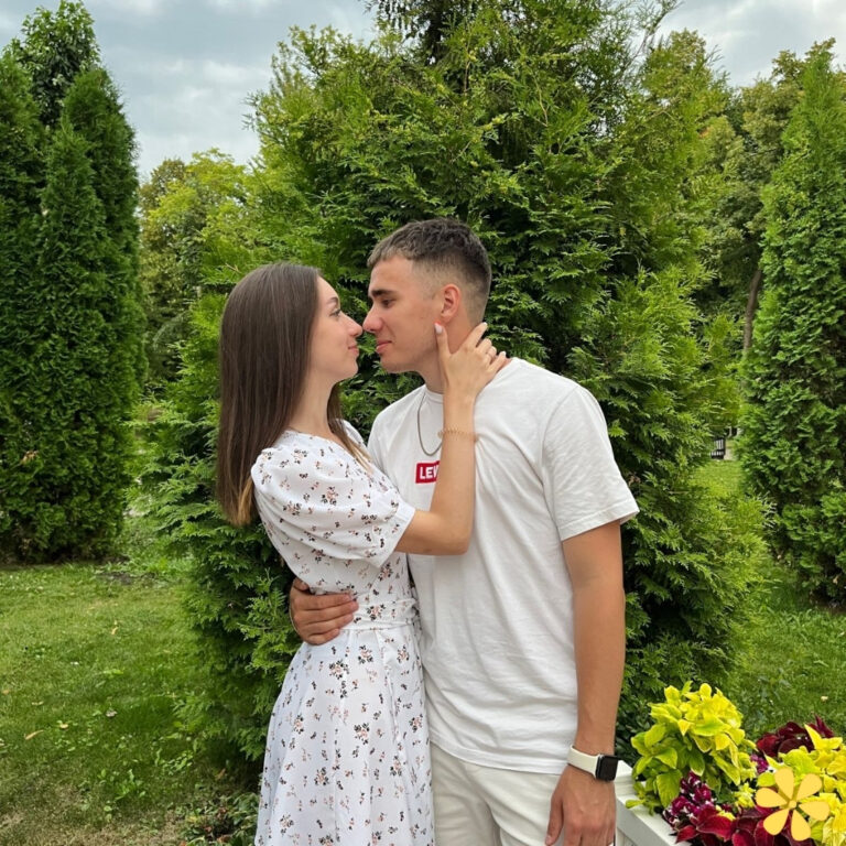 Young couple sharing a tender moment outdoors, framed by lush greenery.