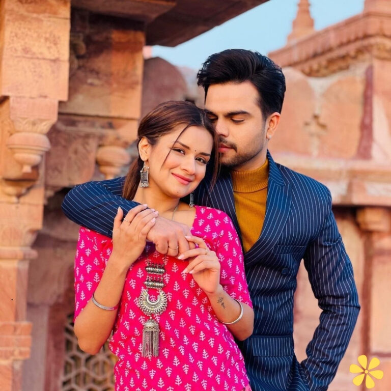 Couple poses warmly, with the man gently leaning in close to the woman, who smiles brightly in a vibrant pink outfit.