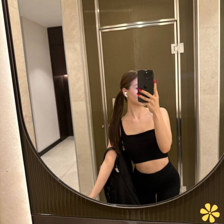 A person takes a selfie in a mirror, wearing a black crop top and leggings.