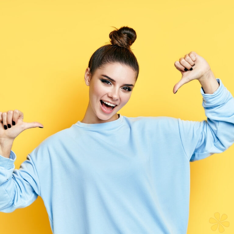 Young woman in a blue sweater gives a thumbs down against a yellow background.