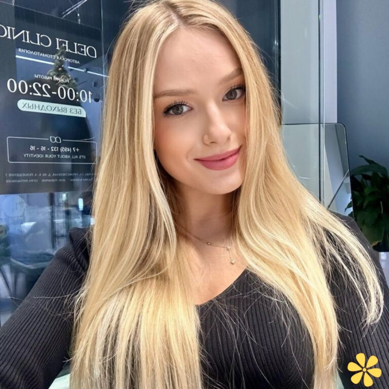 A young woman with long blonde hair smiles warmly at the camera, showcasing her relaxed style.