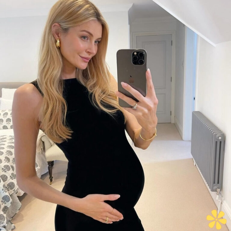 Expectant mother in black dress holds her baby bump, smiling softly at her reflection.