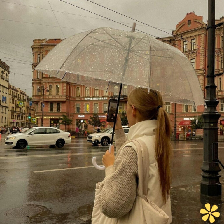 A person with a clear umbrella stands in the rain, gazing at the cityscape.