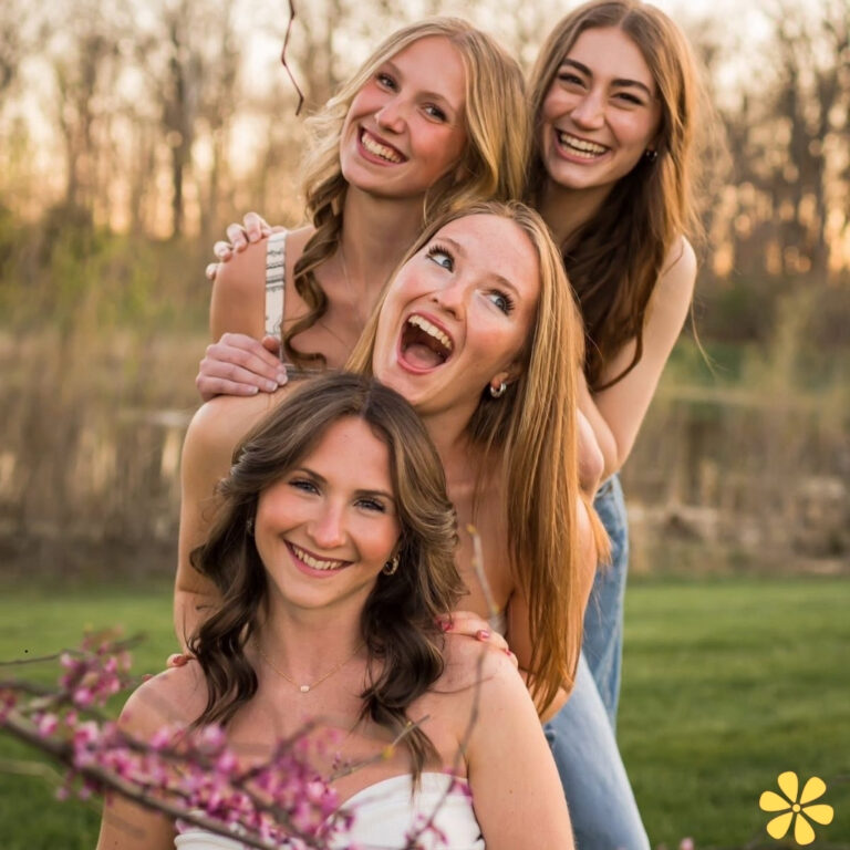 Four friends posing joyfully outdoors, smiling brightly at the camera.