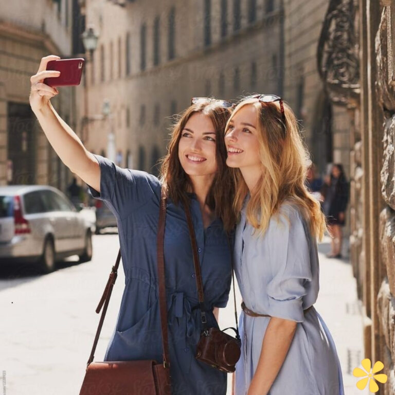 Two women smiling and taking a selfie together in a sunny street.