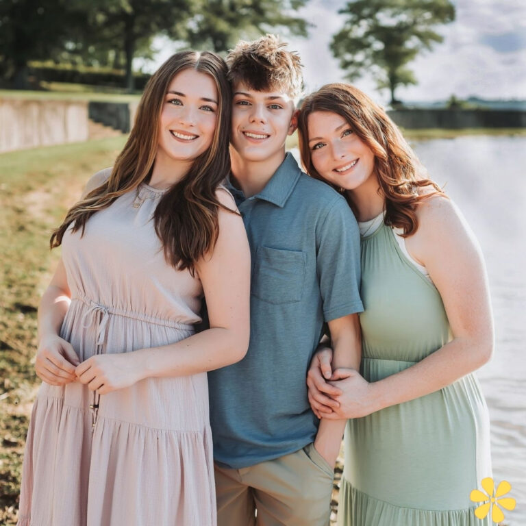 Three friends stand close together by a lake, smiling warmly at the camera.